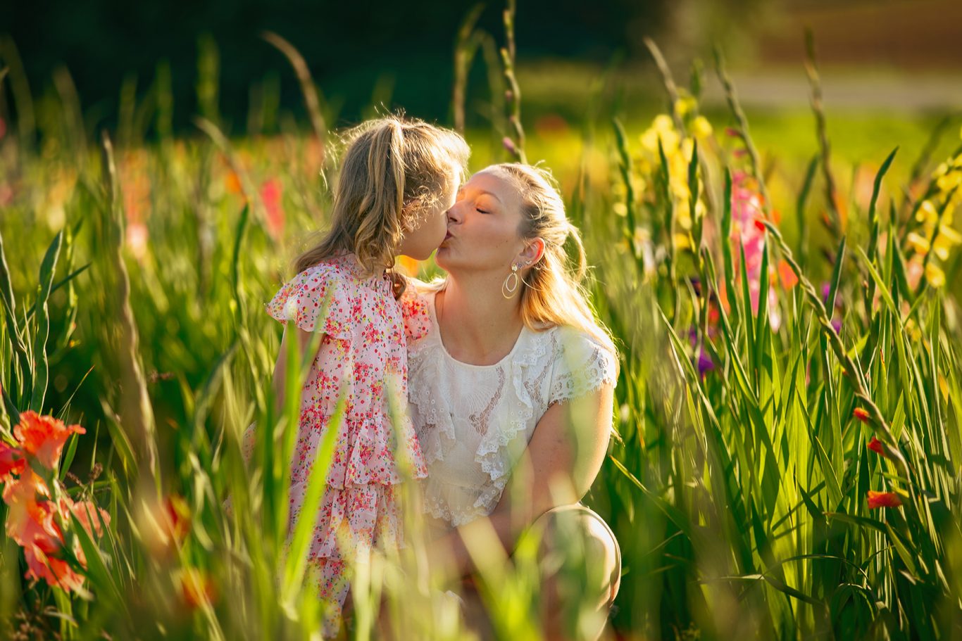 Frau küsst ein Mädchen in einem blühenden Feld voll bunter Blumen.