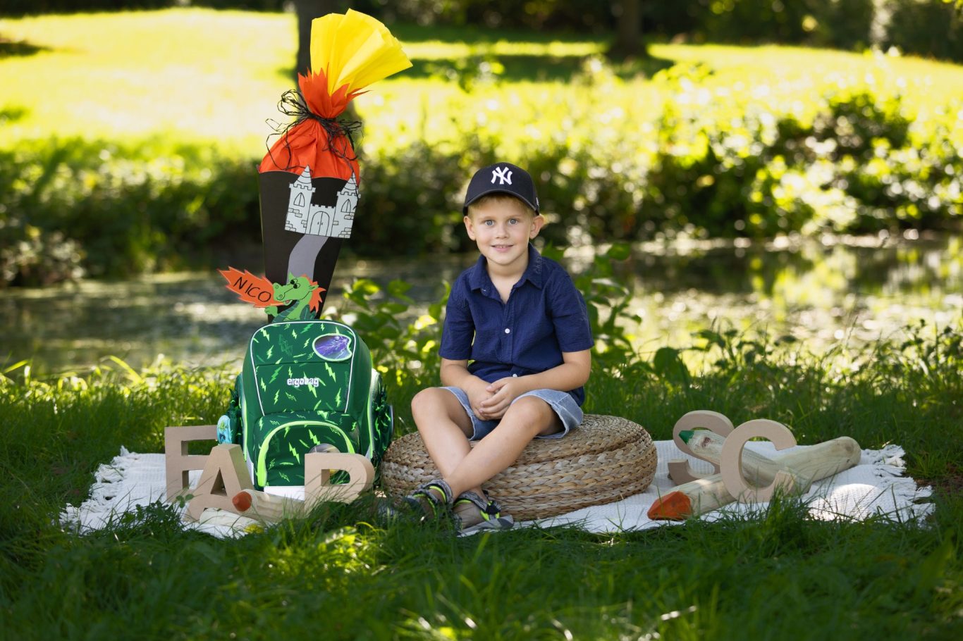 Ein Junge sitzt im Freien neben einem bunten Rucksack und Dekoration auf dem Gras.